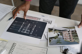 Draufsicht auf einen Schreibtisch, an dem ein Architekt Entwürfe und Fotos eines modern begrünten Wohngebäudes sichtet