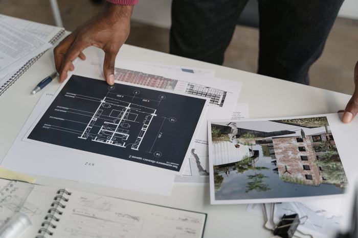 Draufsicht auf einen Schreibtisch, an dem ein Architekt Entwürfe und Fotos eines modern begrünten Wohngebäudes sichtet